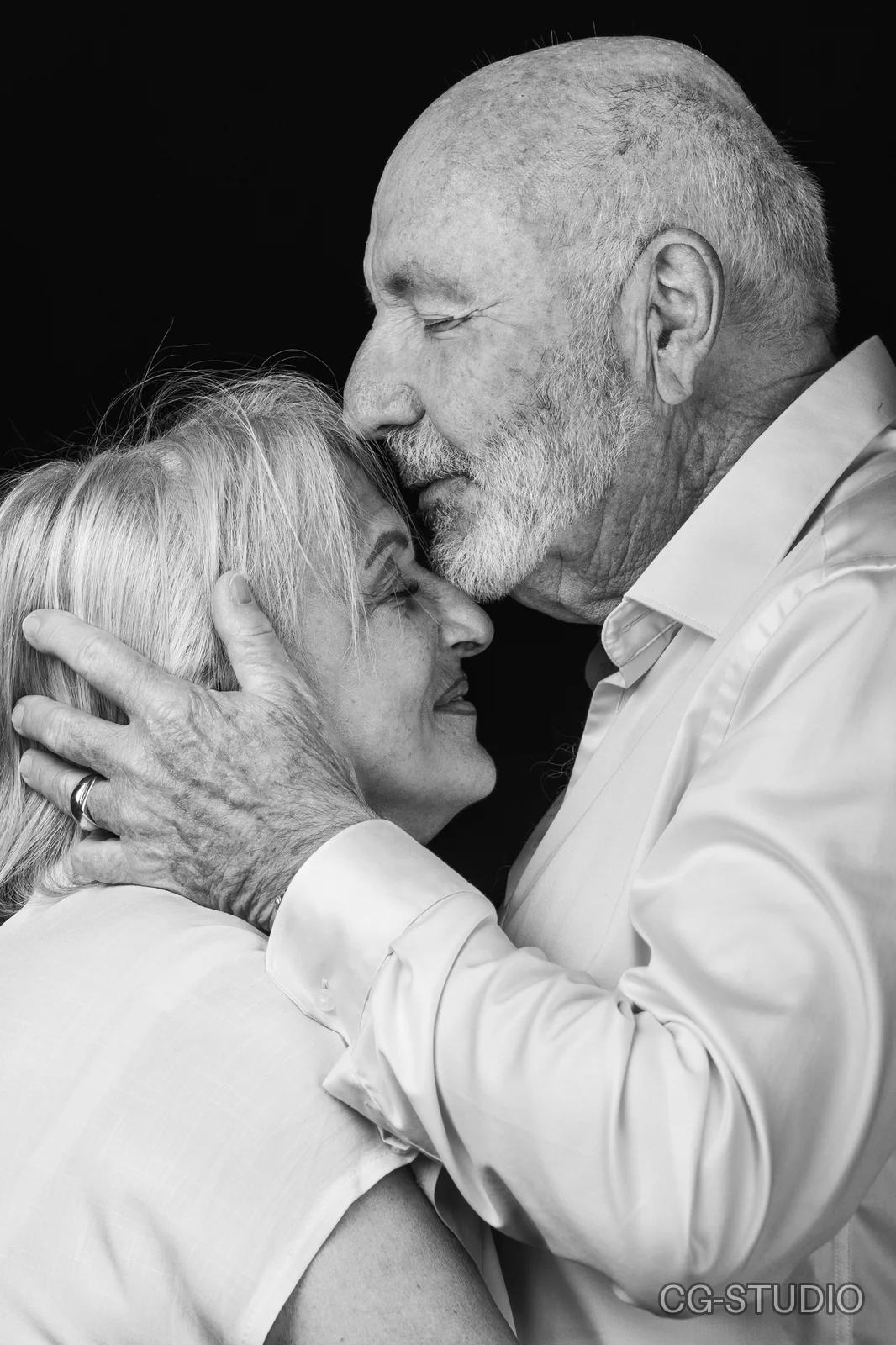Homme âgé barbu, yeux clos, embrassant le front d'une femme souriante qu'il tient par la nuque, noir et blanc sur fond noir