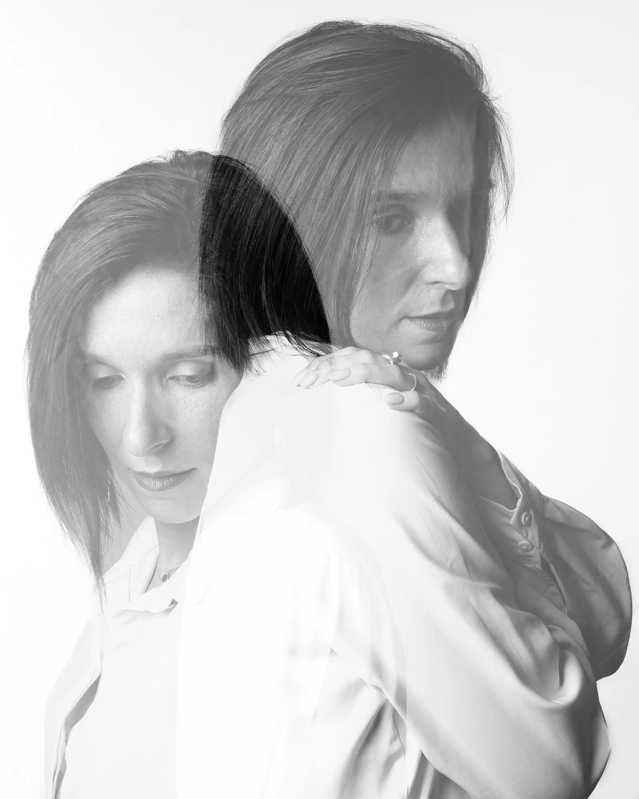 Double exposition en noir et blanc d'une femme aux cheveux mi-longs, chemise blanche, main sur son épaule, regard baissé