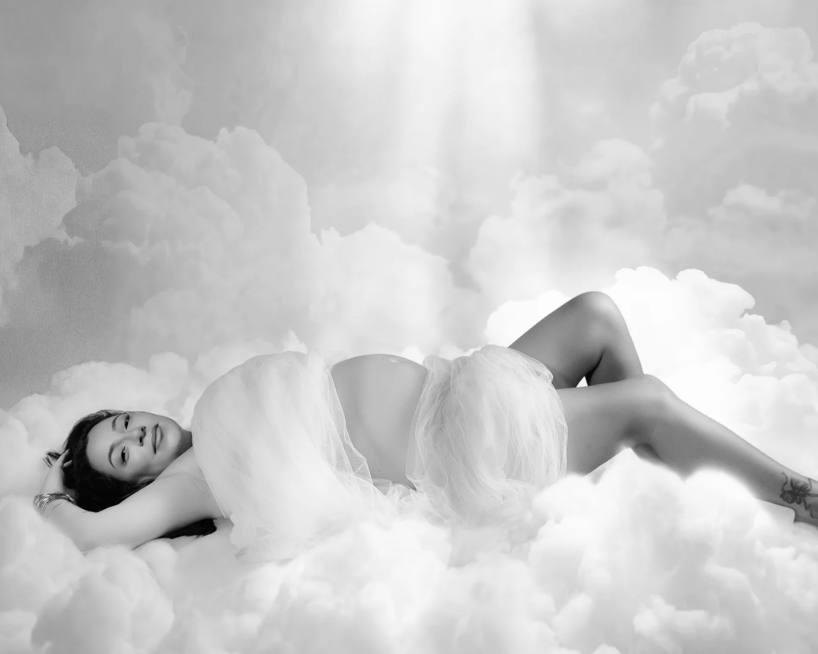 Femme enceinte allongée sur des nuages, ventre nu entre deux voiles de tulle, rayon de lumière venu d'en haut, noir et blanc